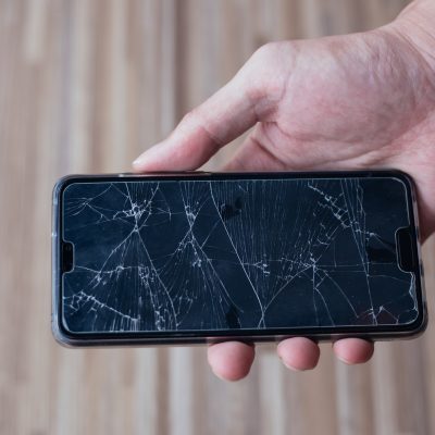 Close-up of human hand holding a broken and damaged glass of mobile phone from accident.